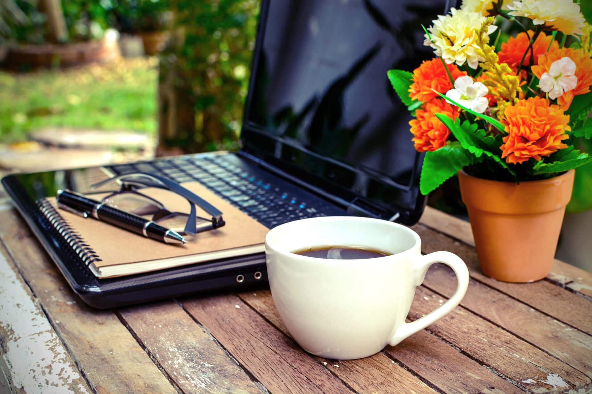 A laptop on a table with a cup of coffee and flowers